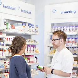 Bilde fra apotek&#58; en kunde og en apotekansatt står og snakker ved en butikkhylle
