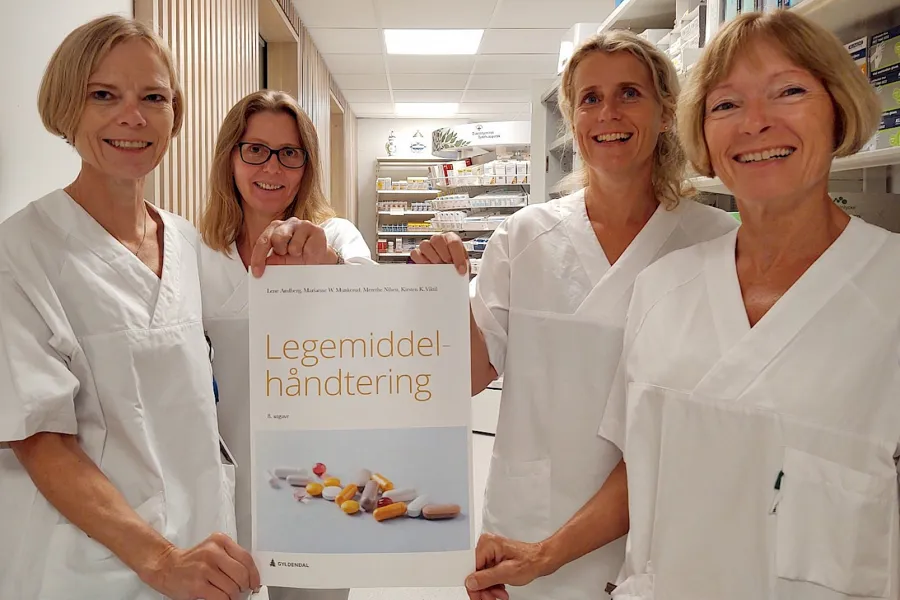 En gruppe kvinner iført hvite laboratoriefrakker som holder et skilt