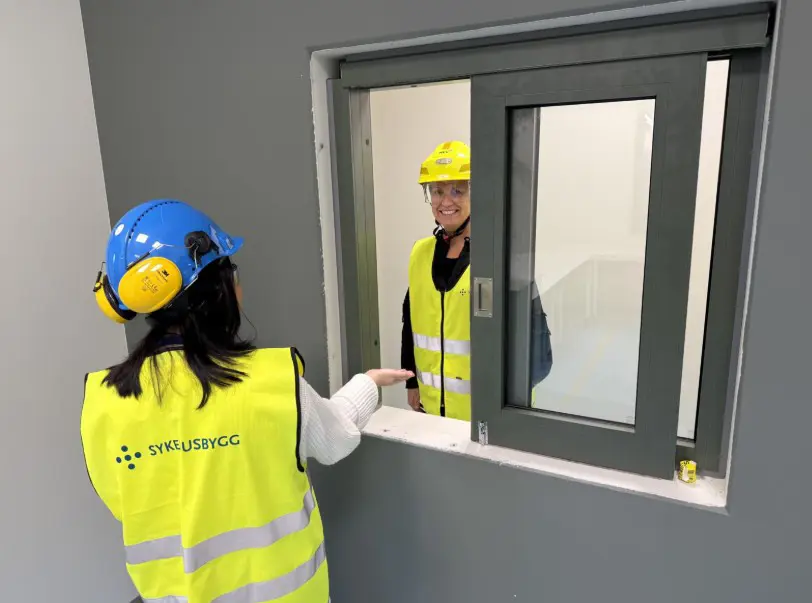 Et par personer med hjelmer og reflekser som ser på et vindu